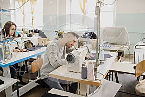 Young man and other seamstresses sewing with sewing machine in a factory