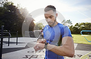 Young man at outdoor gym setting fitness app on smartwatch