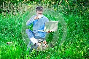 Young man outdoors with a cup and laptop