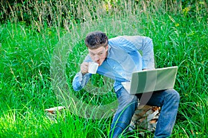 Young man outdoors with a cup and laptop
