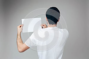 Young man  over background. Back view of guy in white shirt hold blank page in hands on left side. Brunette man