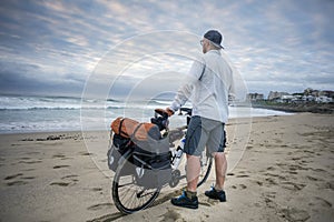 Young man with packed bicycle on beach