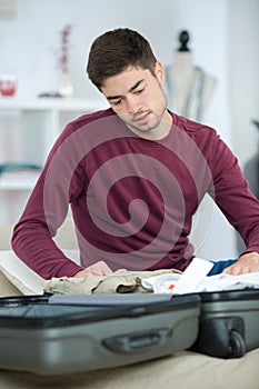 Young man packing clothes into travel bag