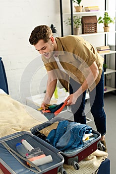 young man packing clothes into travel bag