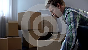 Young man packing things in cardboard boxes, moving from dormitory to own house