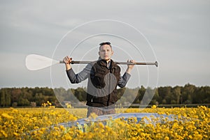 A young man with a paddle and sup Board in a rapeseed field