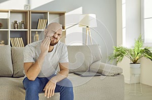 Young man with painful expression holds his cheek suffering from severe toothache.