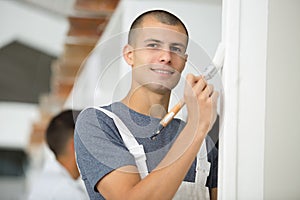 young man painter in uniform painting white wall