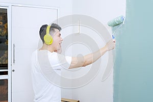 Young man painting interior wall with paint roller