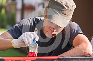 Young man is painting metal fence with a brush
