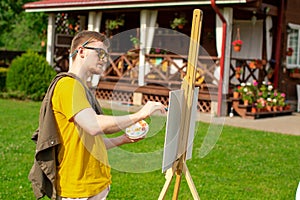 Young man paints painting outside his country house. Summer open air session