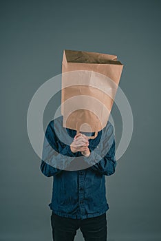 Young man with a paper bag on his head, hands fold for praying, hope concept