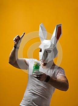Young man in paper rabbit mask and white t-shirt drinking green cocktail drink