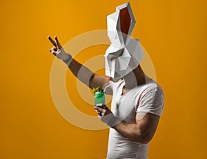 Young man in paper rabbit mask and white t-shirt drinking green cocktail drink