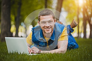 Young man in the park lying on grass with laptop