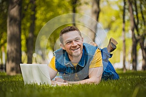 Young man in the park lying on grass with laptop