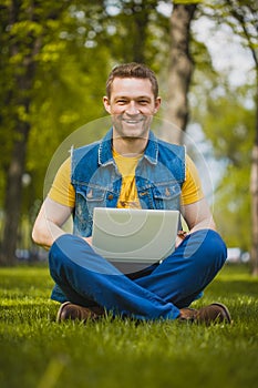 Young man in the park lying on grass with laptop