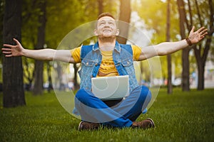 Young man in the park lying on grass with laptop