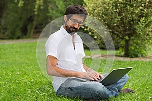 Young man in the park sitting on the grass with a laptop