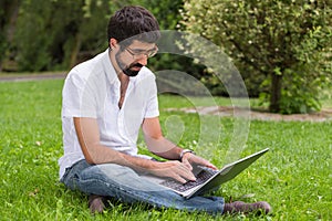 Young man in the park sitting on the grass with a laptop