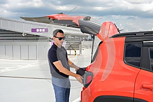 Young man in a parking lot puts his suitcase in the trunk of a car.