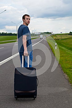 The young man pending on road with suitcase