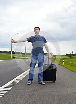 The young man pending on road with a suitcase