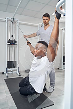 Young man performing stretching exercise assisted by physical therapist