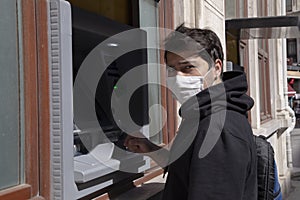 The young man performs his transactions from the bank atm using his protective mask