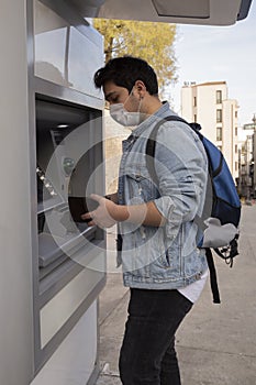 The young man performs his transactions from the bank atm using his protective mask