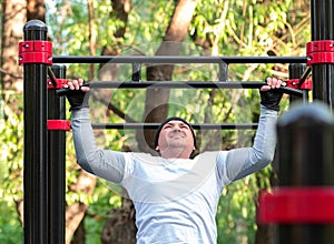 The young man performs a sports exercise pull-up on the bar. Training on the street to develop the strength of the back muscles, photo