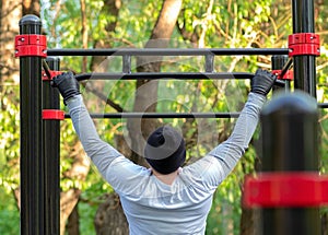 A young man performs a sports exercise pulling on the simulator crossbar. Outdoor training develops the strength of the back photo