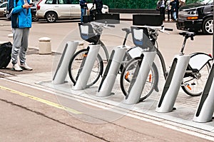 A young man in a phone and a suitcase stands near the bike park. Bicycle for rent photo