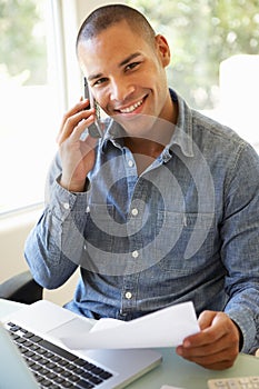 Young Man On Phone Using Laptop At Home