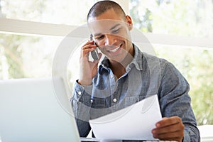 Young Man On Phone Using Laptop At Home