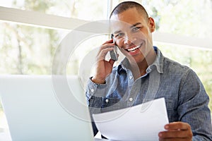 Young Man On Phone Using Laptop At Home