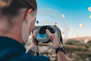 Young man photographer making pictures of air balloons at sunrise time in Cappadocia