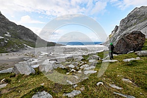 Young man photographer standing at rock in the mountains at Bunes Beach photographing the landscapes on Lofoten Islands in Norway.