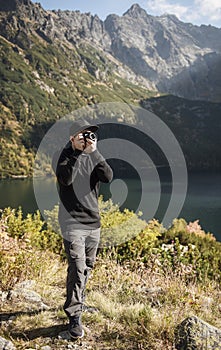 Young  man photographer taking photographs with digital camera in a mountains