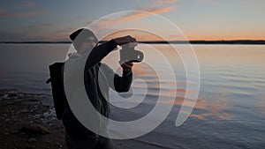 Young man photographer taking pictures with a professional camera by the Torrevieja Pink lake at sunset