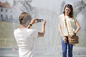 Young man photographing woman against fountain