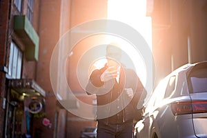 Young man photographs himself against backdrop of modern buildings in city.