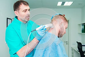 Young man at the physiotherapy receiving laser therapy massage. A chiropractor treats patient`s cervical spine in medical office.