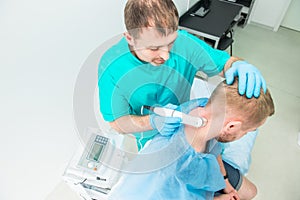 Young man at the physiotherapy receiving laser therapy massage. A chiropractor treats patient`s cervical spine in medical office.