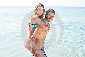 Young man piggybacking girlfriend on shore at beach