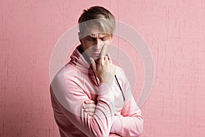 Young man in a pink hoodie thinks about the problem, a portrait of a guy on a pink background