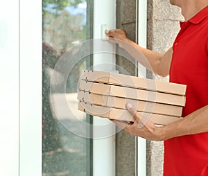 Young man with pizza boxes ringing the doorbell outdoors. Food delivery service