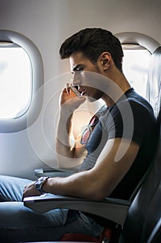 Young man in plane talking on cell phone