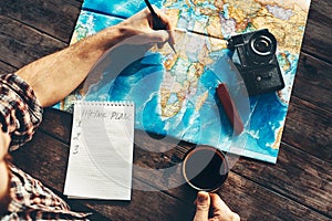 Young Man Is Planning Vacation Travel With Map, Top View. He Drinks Coffee And Marks