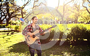 Young man playing acoustic bass guitar in the park